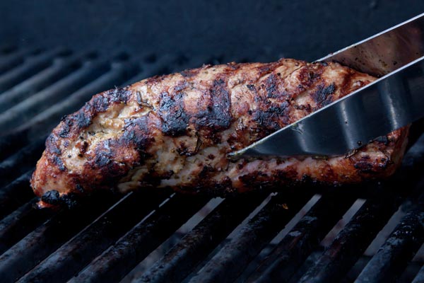 Pork tenderloin with tongs on a hot grill